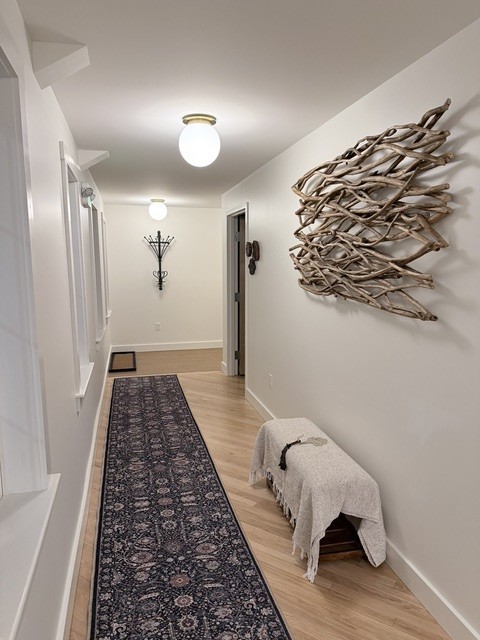 The entry hallway at Gather Wellness Center, with a long patterned runner, a blanket-draped bench, globe ceiling lights, and a large driftwood wall sculpture.
